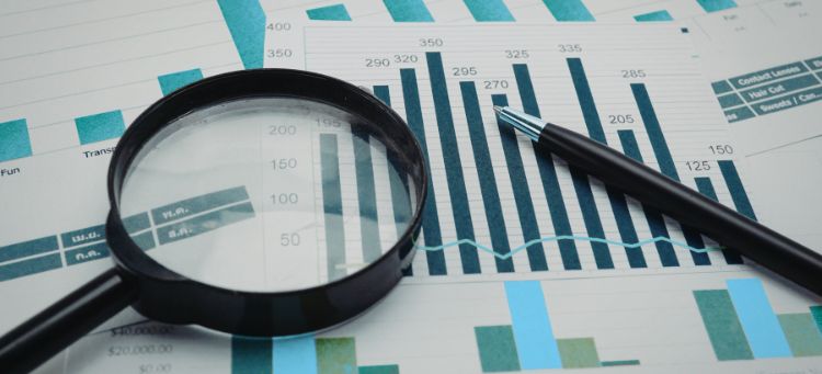 Auditoria Interna representada por uma lupa e gráficos de barra impressos sobre a mesa de uma empresa