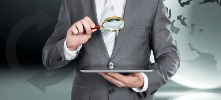 Auditor avaliando com uma lupa num tablet o Impacto Estratégico das Novas Normas Globais de Auditoria Interna