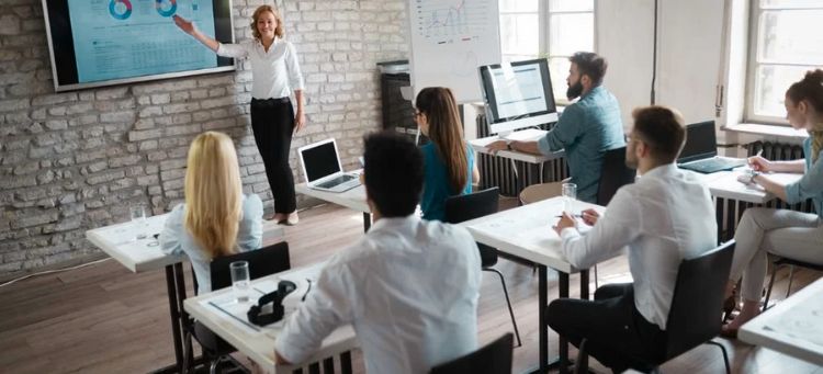 Instrutora realizando o treinamento de liderança em uma sala exibindo informações em um monitor